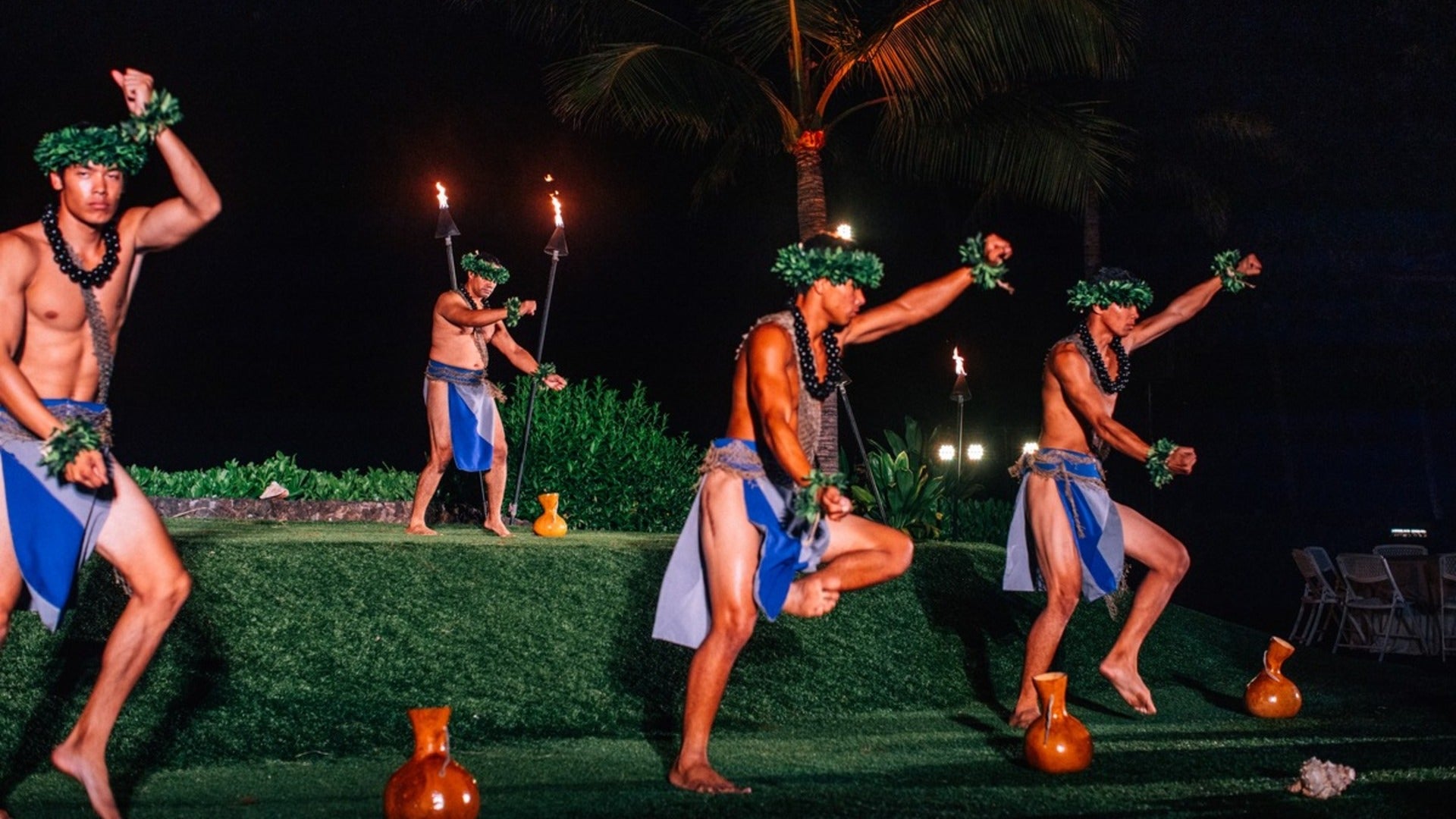 hawaiian male dancers in a luau with torches behind and trees